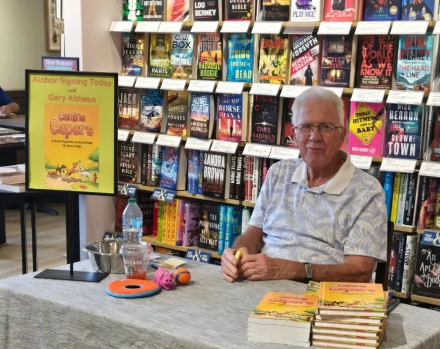 Gary Althaus seated at the Barnes & Noble signing table beside a Canine Capers sign and stacks of books.